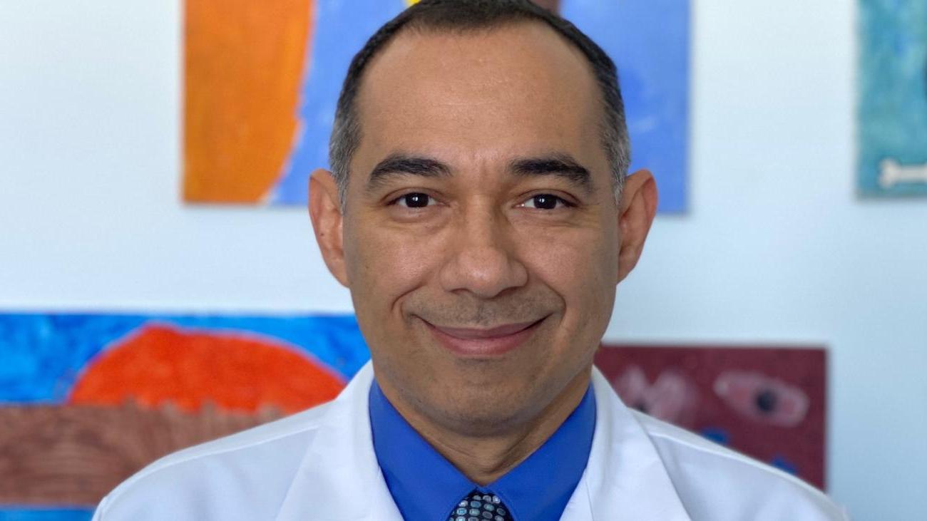 Dr. Edgar Chavez '98 in medical white coat in front of colorful background